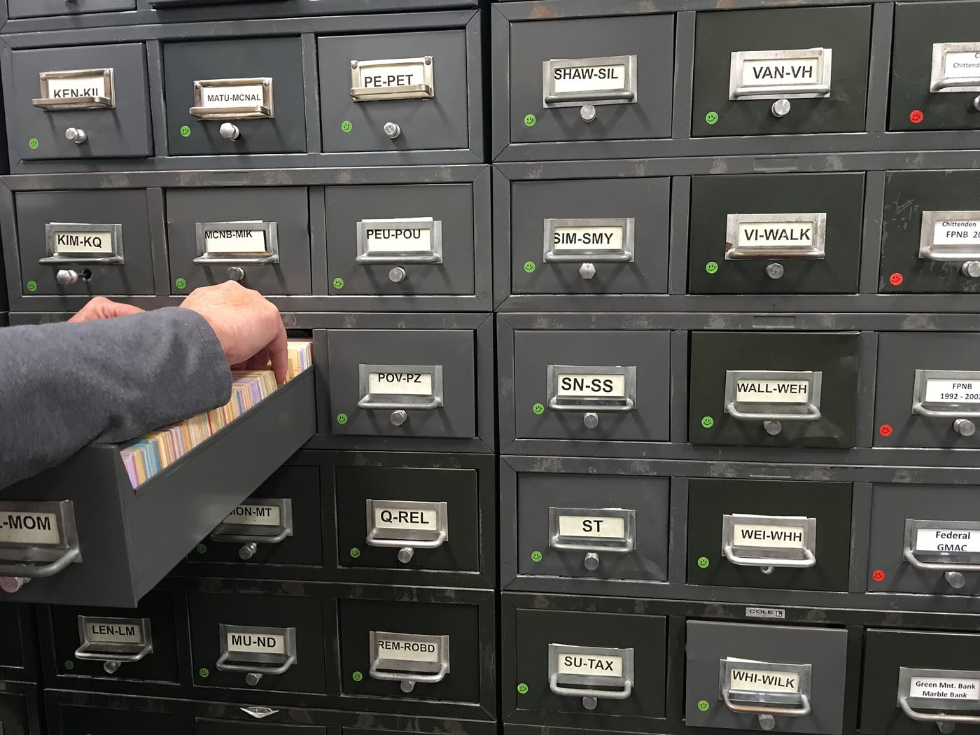 Wall of labelled card-catalog drawers in a records office, one drawer pulled open